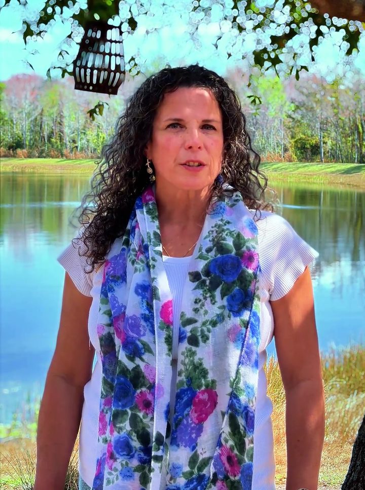 Judy Willemsen standing beside a Central Florida lake, wearing a white top and a floral scarf